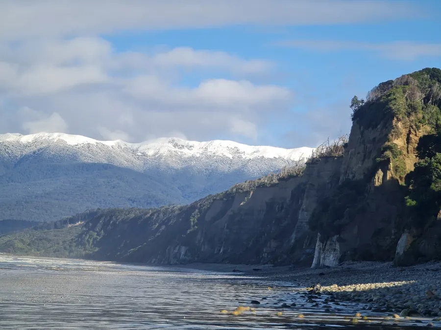 The cliffs of Bluecliffs Beach with snow on the hills behind