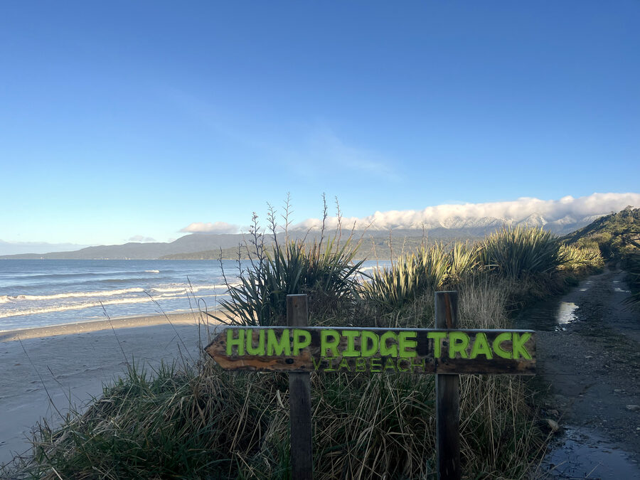 The Hump Ridge Track sign pointing the way via the beach, snow on the tops behind