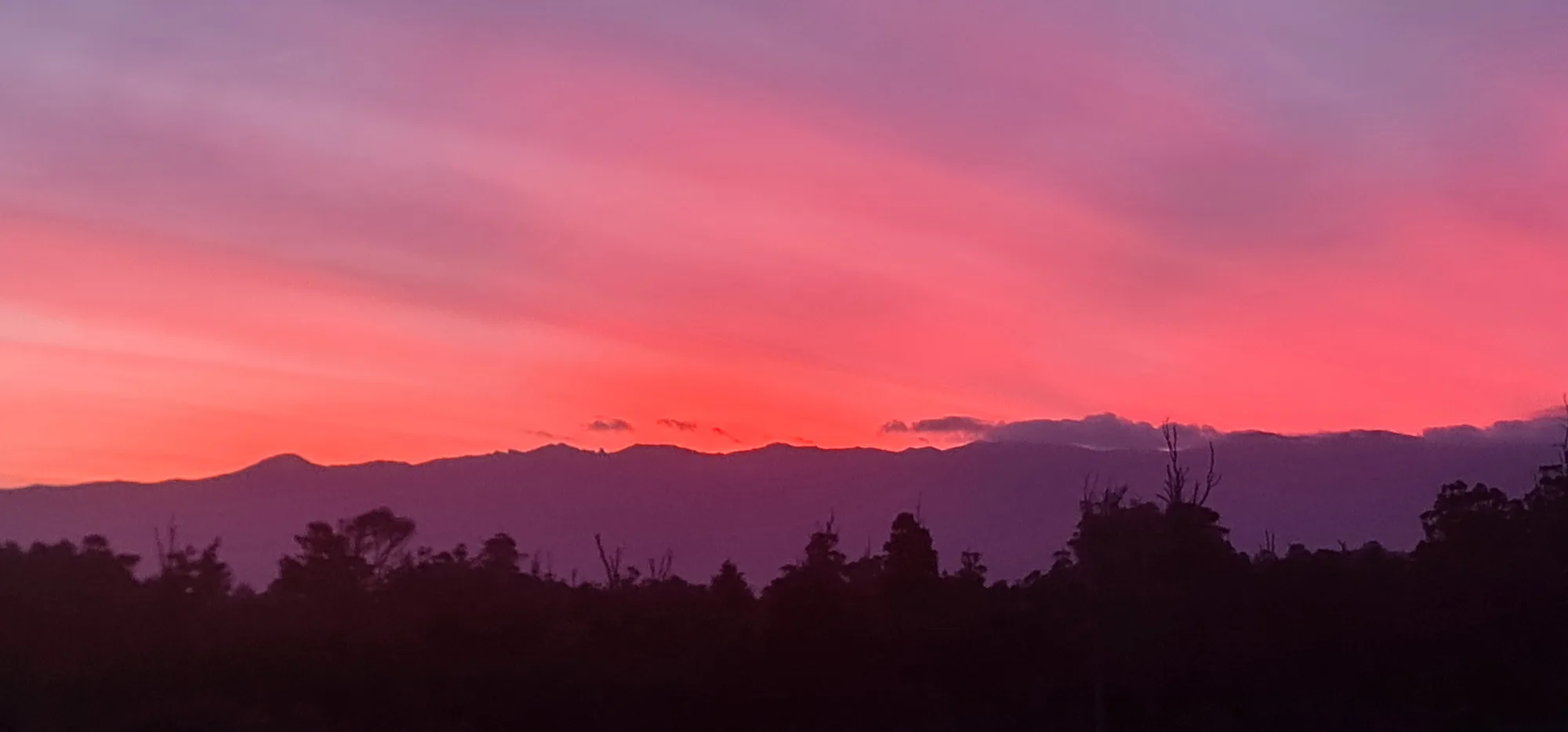 Pink and red sunset sky behind the Hump Ridge, seen from Rarakau Lodge